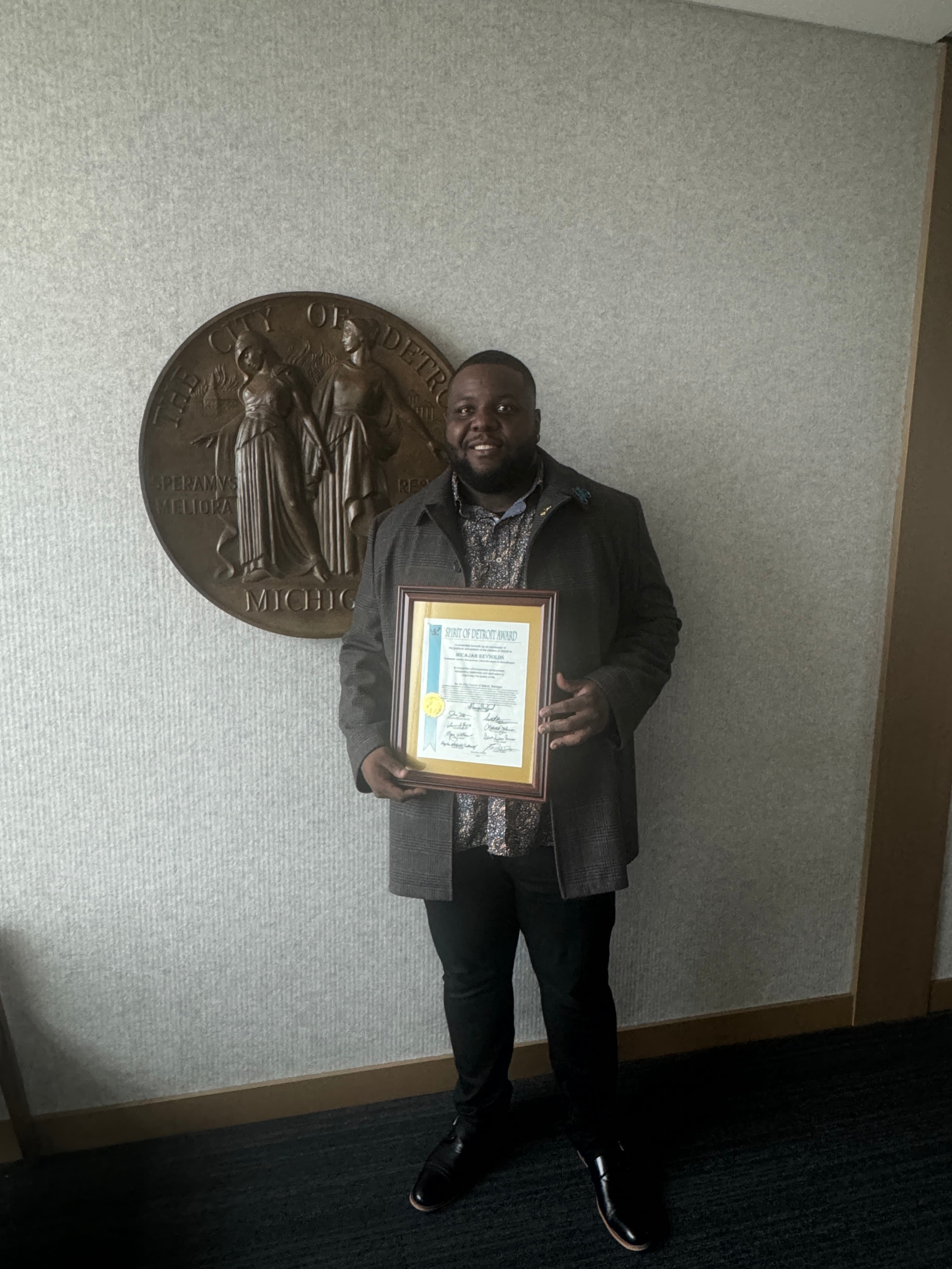 Caj Reynolds holding his Spirit of Detroit award in front of the City of Detroit seal